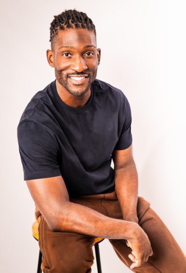 Friendly close-up studio portrait of a smiling man wearing a dark T-shirt against a light background.